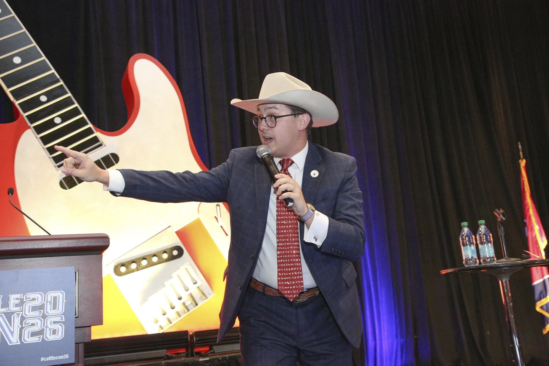 Tanner Beymer calling bids on stage in front of the giant guitar at CattleCon